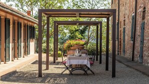An outdoor patio with a pergola, a table set for dining, and a flower pot with red flowers. - Apartment with 2 bedrooms and 2 bathrooms on the ground floor (Toscana)