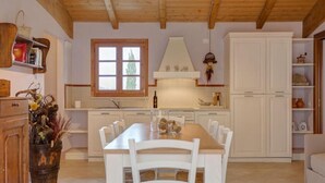 A kitchen with white cabinets, a wooden dining table, and chairs. There is a window with a view of trees outside. - Apartment with 2 bedrooms and 2 bathrooms on the ground floor (Toscana)