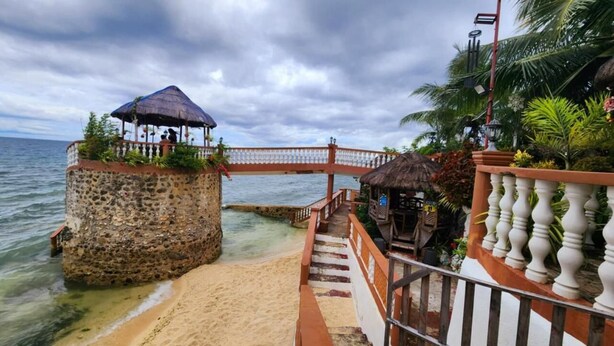 A stone structure with a thatched roof and a wooden bridge leading to a beach. - Torre De Alcoy by Hiverooms (Alcoy)