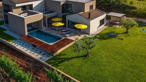 A modern multi-story house with a swimming pool, outdoor seating, and a well-maintained lawn.