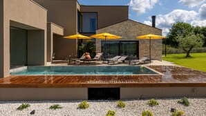 A modern pool area with lounge chairs and umbrellas, a stone building, and a clear sky.