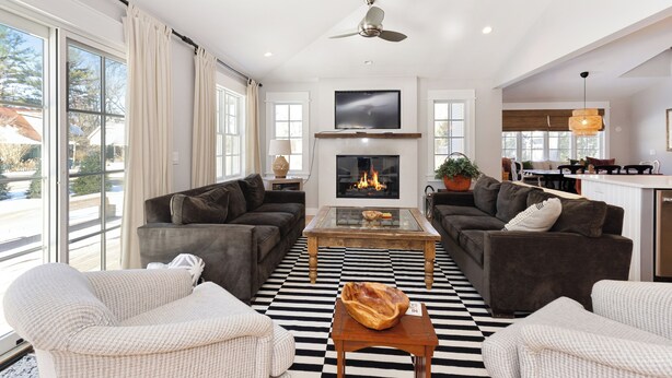 A spacious living room with a fireplace, two sofas, a coffee table, and a large window overlooking a snowy landscape. - 500 FT To Beach, Main House, Guest House, Fire Pit (Union Pier)