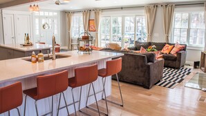 A modern kitchen with a central island, bar stools, and a seating area with a sofa and cushions. - 500 FT To Beach, Main House, Guest House, Fire Pit (Union Pier)
