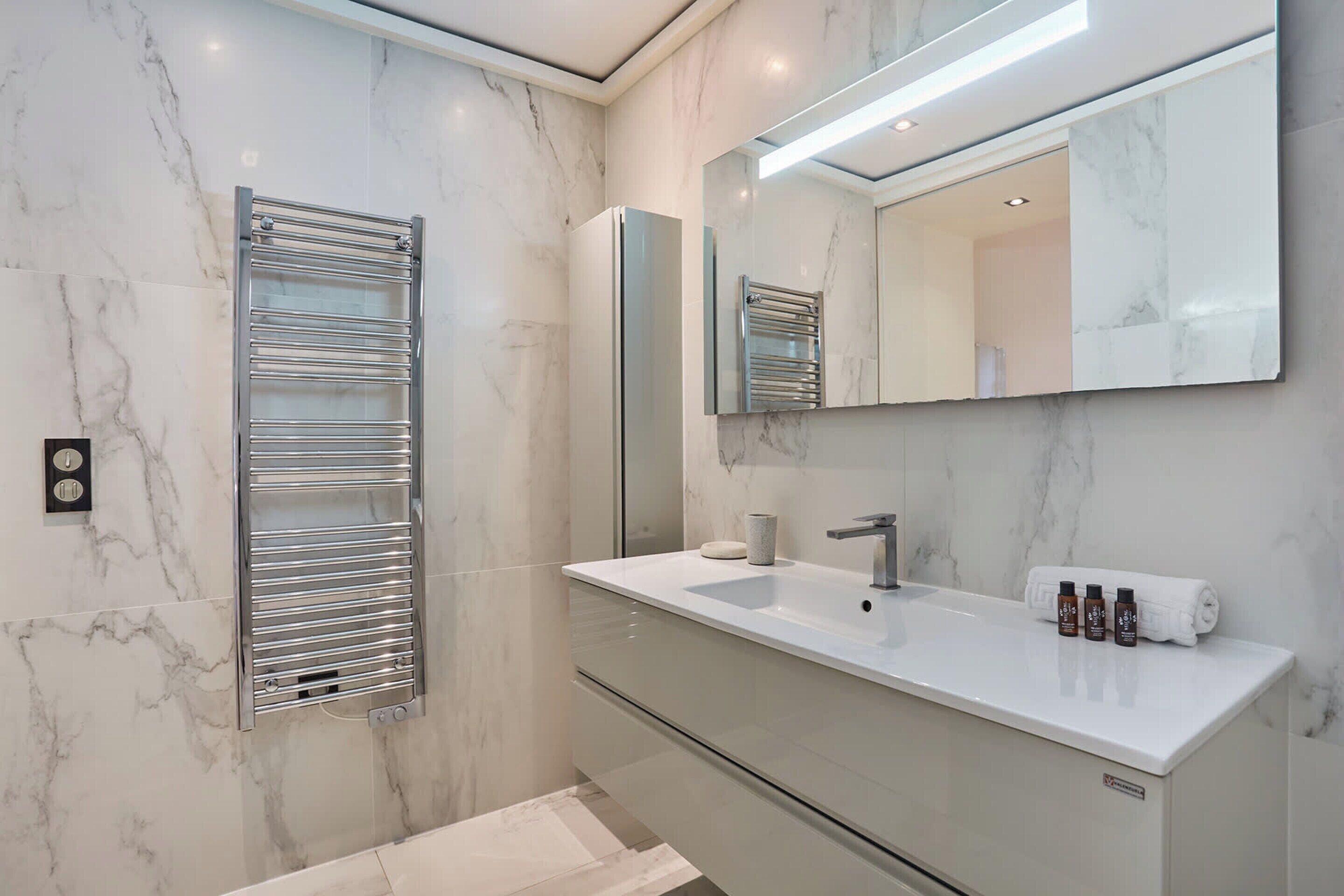 Ein modernes Badezimmer mit Marmorwand, integriertem Waschbecken, Spiegel und Handtuchhalter.