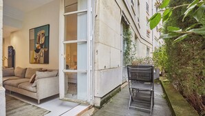 An open-plan living area with a sofa, a painting, and a bench outside. - Appartement Centre de Paris Le Marais (Paris)