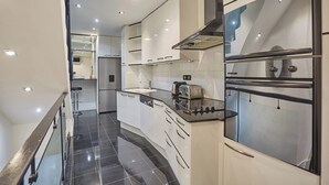 A modern kitchen with white cabinets, a black countertop, and a stainless steel range hood. - Appartement Centre de Paris Le Marais (Paris)