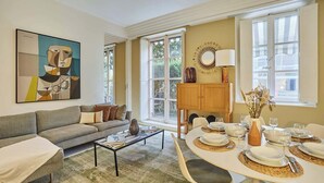 A living room with a sofa, coffee table, and dining area with a table set for four. - Appartement Centre de Paris Le Marais (Paris)