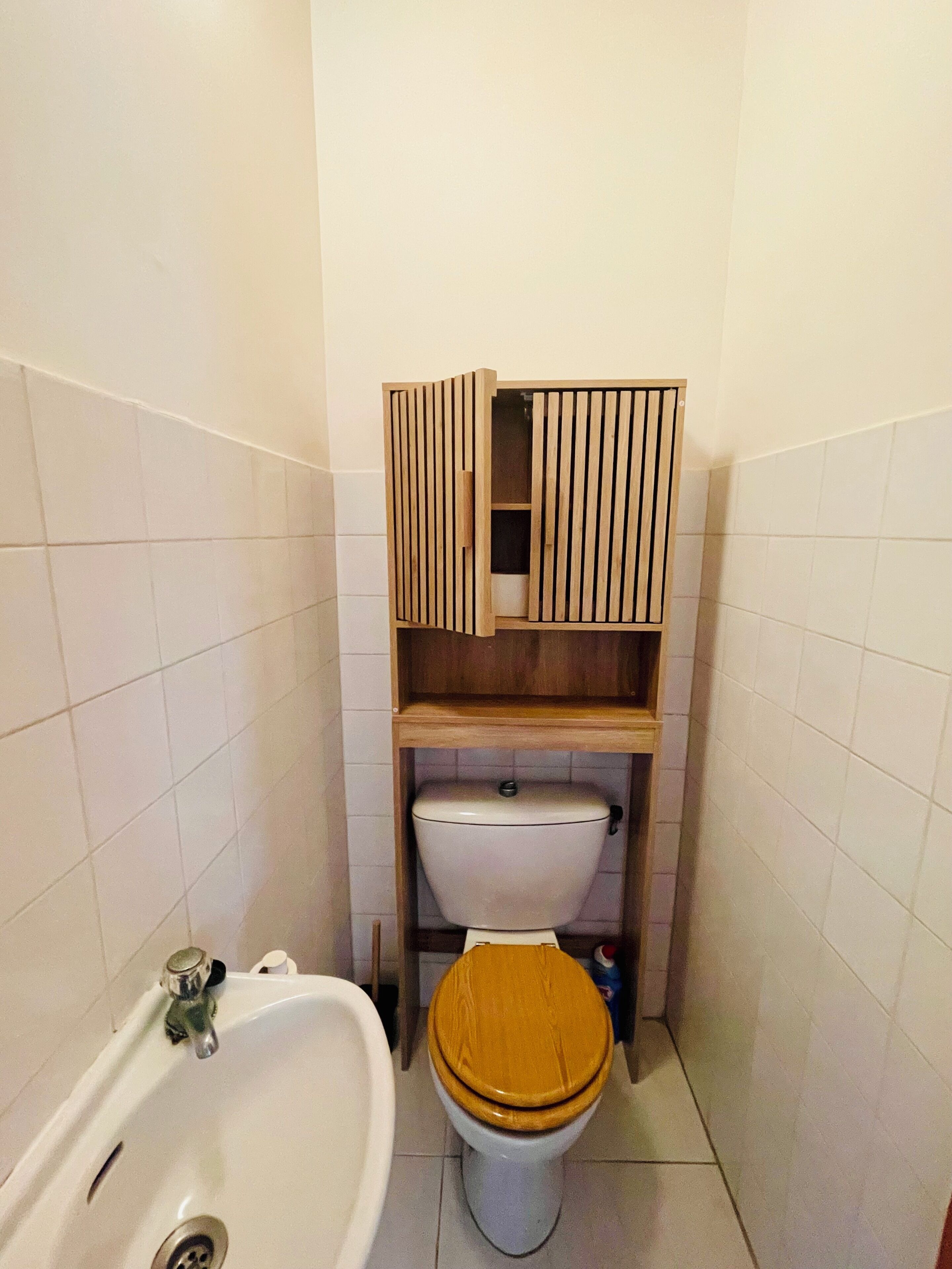 Un bagno piccolo con il water, un mobiletto in legno sopra il water e una vasca.