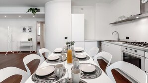 A modern kitchen with white cabinetry, a built-in stove, and a dining area with a white table set for four. - Bright & Modern 2-Bedroom Apartment in a Quiet Location (Milano)