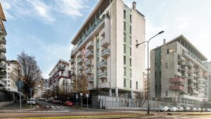 A multi-story residential building with balconies, a parking area, and a street view. - Bright & Modern 2-Bedroom Apartment in a Quiet Location (Milano)