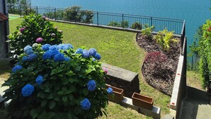 Une vue sur un lac avec des montagnes en arrière-plan, un balcon orné de plantes en pot et un mur de pierre.