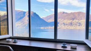 Une pièce dotée d’une grande fenêtre donnant sur un lac et des montagnes. On y trouve une table sur laquelle sont posés une tasse et un bol.