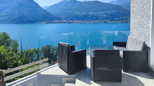 Un balcon doté de meubles en osier, offrant une vue sur un lac et des montagnes.