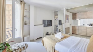 A modern hotel room with a bed, bedside table, and a small sitting area. There is a kitchenette in the adjacent room. - Studio Montaigne/ Champs Elysees (Paris)