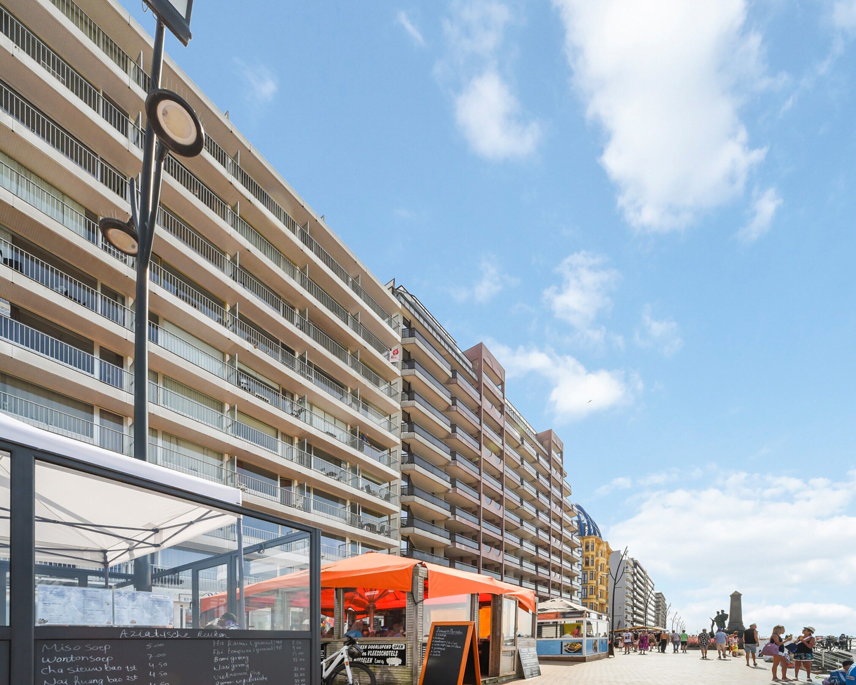 A multi-story hotel with balconies, a street vendor area, and a clear sky.