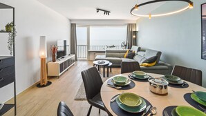 Una sala de estar moderna con comedor, un sofá, televisor y un balcón con vistas.