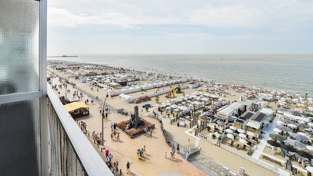 Vista de la playa con paseo marítimo, sombrillas y un puerto deportivo.