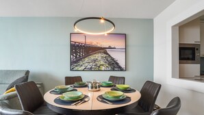 Un comedor con una mesa redonda, sillas negras y un cuadro de un muelle.