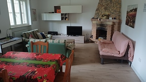 Una sala de estar con chimenea, televisión, una mesa de comedor con mantel floral y un sofá con cubierta a rayas.
