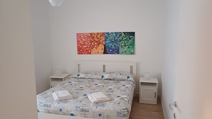 Un letto rifatto con copriletto decorato, due comodini e un quadro astratto dai colori vivaci sopra il letto.