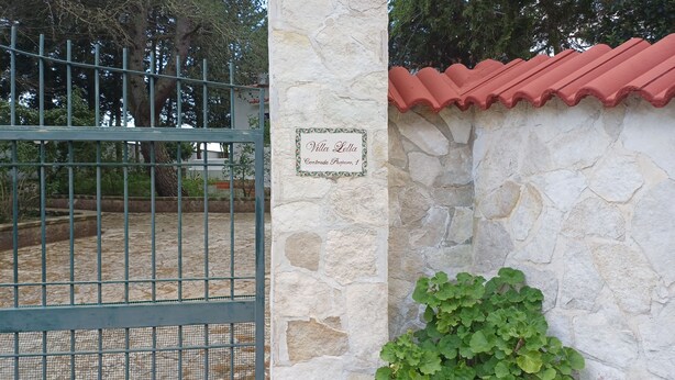 Un muro in pietra con un cartello, un cancello in metallo e un tetto in tegole rosse.