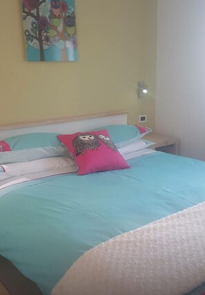 Un lit recouvert d’une couvre-lit turquoise, agrémenté d’oreillers roses et blancs, et orné d’un tableau représentant des hiboux accroché au mur.