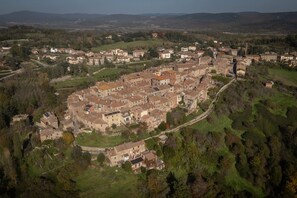 An aerial view of a historic town with a central square, surrounded by buildings with traditional architecture, and a hilly landscape in the background.