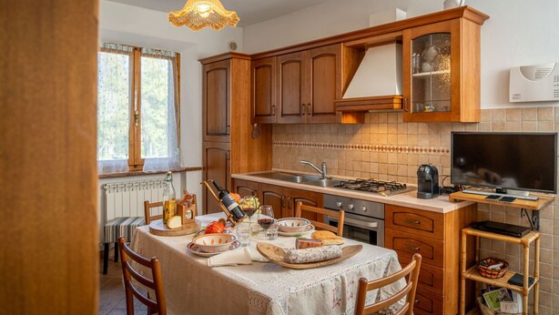 Una cocina con armarios de madera, una mesa de comedor dispuesta con platos, vasos y una botella de vino.