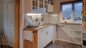 Een compacte keuken met witte kastjes, een houten aanrecht, een spoelbak en een raam met uitzicht.