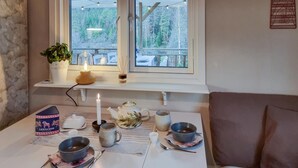 Een eethoek met een tafel gedekt voor twee personen, een kaars, een theepot en een potplant.
