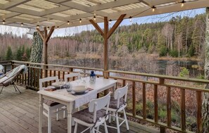 Comedor con una mesa preparada para cuatro, con vistas a un área boscosa y una masa de agua.