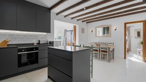 A modern kitchen with dark cabinetry, a central island, and a dining area with a wooden table and chairs. - Apartment With Roof Terrace and Pool - Ref 129 (Mijas)