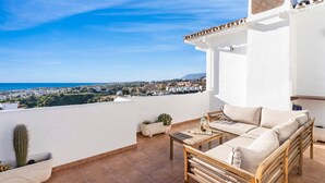 A balcony with a white wall, a wooden sofa, a small table, and a cactus plant. - Apartment With Roof Terrace and Pool - Ref 129 (Mijas)