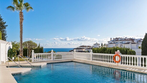 A swimming pool with a white fence, a palm tree, and houses in the background. - Apartment With Roof Terrace and Pool - Ref 129 (Mijas)