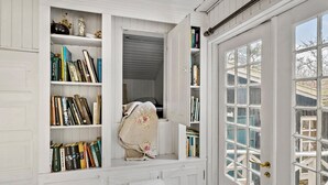 Ein Zimmer mit großem Fenster, einer Bücherwand voller Bücher und einem Bett mit Blumendekorative.