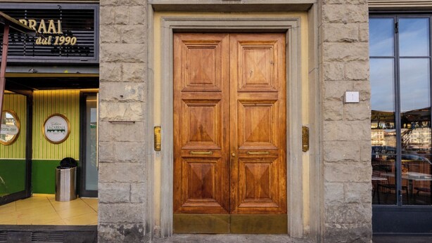 Puerta doble de madera con manija de latón, pared de piedra y un basurero a la izquierda.