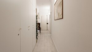 Un pasillo estrecho con paredes blancas, piso de baldosas y una puerta al final.