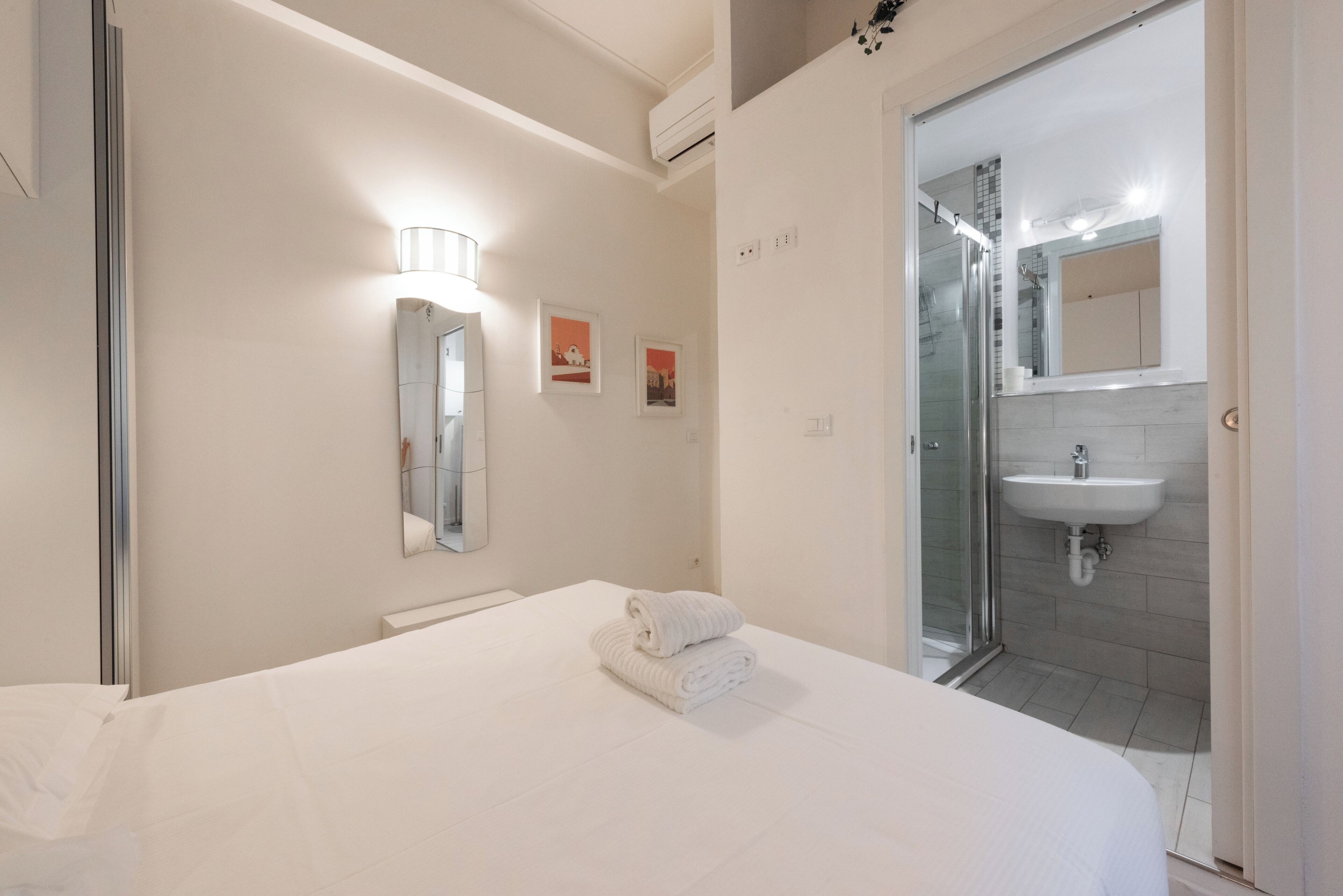 Une chambre d’hôtel avec un lit, une salle de bain dotée d’une douche en verre et d’un lavabo blanc.