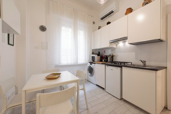 A modern kitchen with white cabinetry, a dining table with chairs, a washing machine, and a microwave.