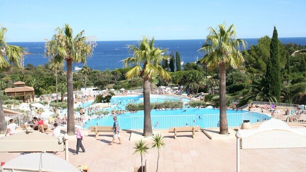 A pool area with palm trees, a view of the sea, and people swimming. - Frisch renoviertes Apartment in traumhafter Lage (Saint-Raphaël)