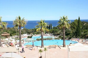 A pool area with palm trees, a view of the sea, and people swimming. - Newly renovated apartment in a dream setting (Saint-Raphaël)