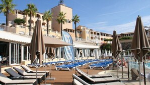 A poolside area with lounge chairs and umbrellas, a pool, and a building with balconies and palm trees. - Frisch renoviertes Apartment in traumhafter Lage (Saint-Raphaël)