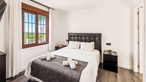 A hotel room with a large bed, a nightstand, a window with a view, and a door. - Villa Elisa (Nerja)