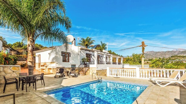 A swimming pool with a tiled deck, surrounded by outdoor furniture and a palm tree. - Villa Elisa (Nerja)