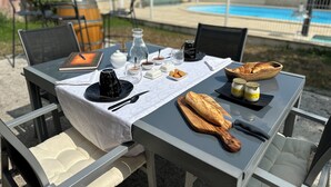 Une table à manger en plein air, sur laquelle on peut voir divers plats, une bouteille et un croissant.