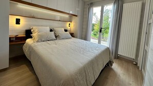 Une chambre à coucher avec un grand lit, des tables de chevet, une armoire intégrée et une fenêtre avec des rideaux.
