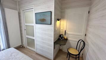 Une chambre à coucher avec un lit, un bureau avec une chaise, un tableau accroché au mur et une porte avec une lumière au-dessus.