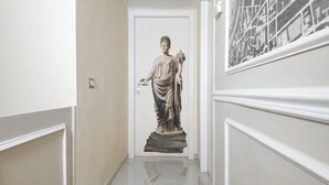 Een gang met een standbeeld van een klassiek figuur, witte muren en een deur.