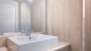 Een badkamer met een witte wastafel, een spiegel en beigekleurige betegelde wanden.