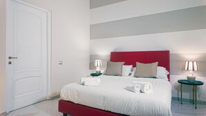 Een keurig opgemaakt bed met witte lakens, een rood hoofdbord en twee nachtkastjes met lampen.